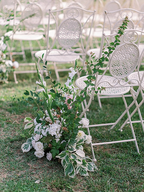 Ceremony seating with outdoor ceremony chairs—white metal chairs lined on a grass lawn, accented by low white flowers and greenery aisle decor