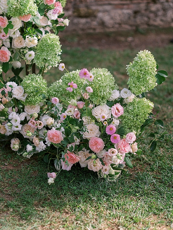 Wedding floral arrangement with hydrangeas and roses in a low pastel ground installation on a grass lawn beside a stone wall