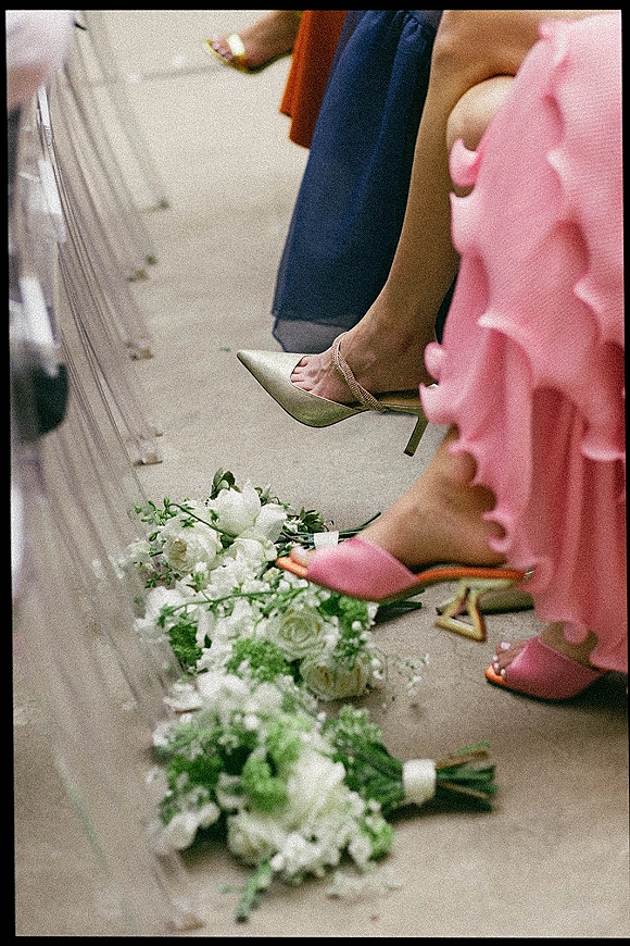 Bridesmaid shoes in pink bridesmaid heels and gold wedding heels, with white rose bouquets by clear acrylic chairs on the aisle