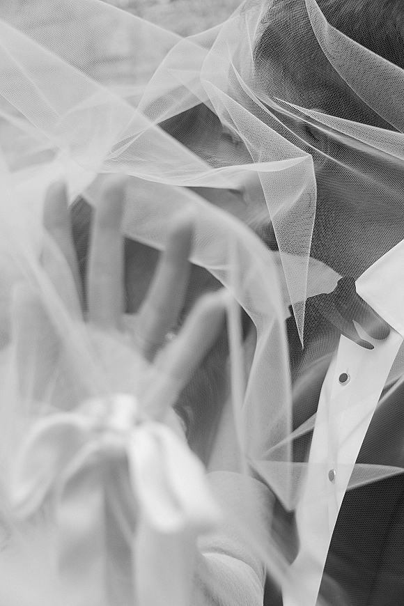 Wedding veil portrait of bride and groom under veil, faces close together through fine tulle, groom in tuxedo against soft blur background