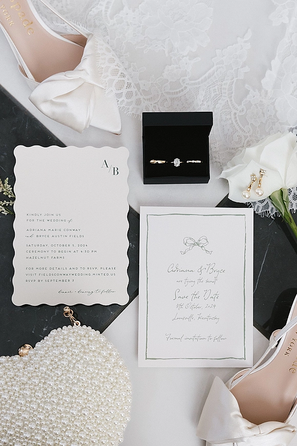 Invitation suite wedding invitation flat lay with save the date, rings in a black box, pearl earrings and white rose on marble surface