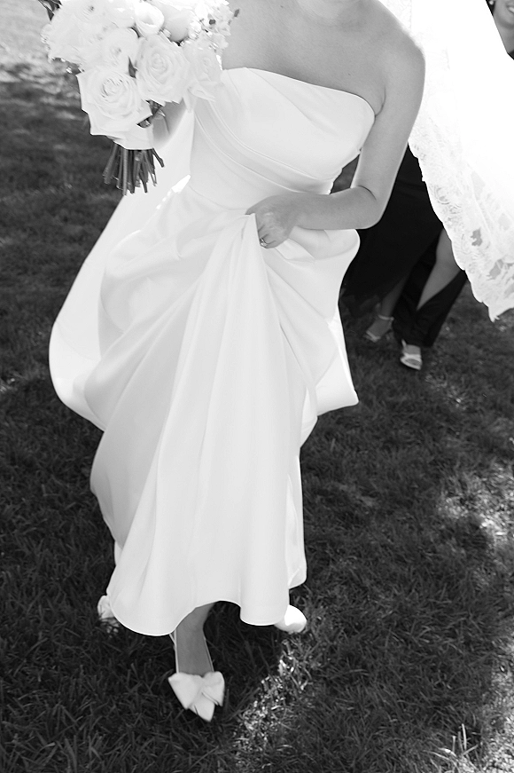 Bride portrait in a black and white bridal photo, lifting her strapless dress while holding a bouquet on a shaded lawn