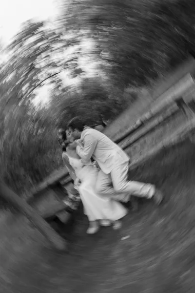 Wedding kiss portrait in black and white as the bride in a simple gown holds a bouquet while kissing her groom on a garden walkway by a stone wall