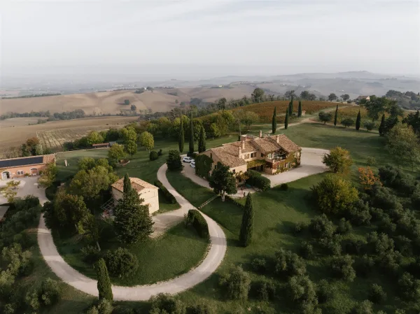 Wedding venue with a stone villa and terracotta roof beside a gravel driveway lined with cypress trees, set amid rolling hills and vineyards