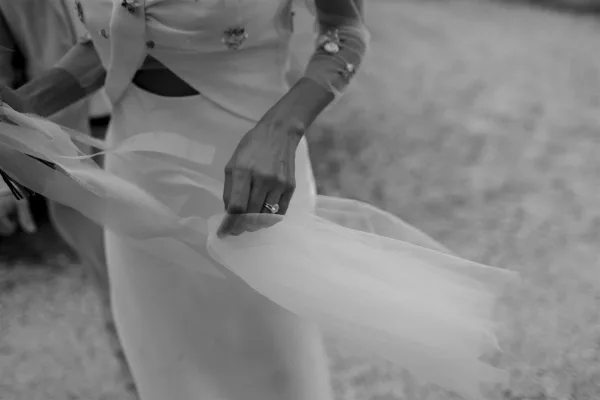 Wedding ring close-up of an engagement ring on hand, bride holding a ribbon against floral-embroidered dress sleeve with blurred greenery background