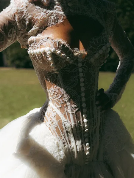 Wedding dress back with illusion back and covered buttons, featuring floral lace embroidery and long sleeves in sunlit greenery outdoors