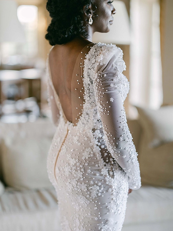 Wedding dress with illusion sleeve wedding dress details, floral lace appliqués and pearl beading, shown low back in window-lit room