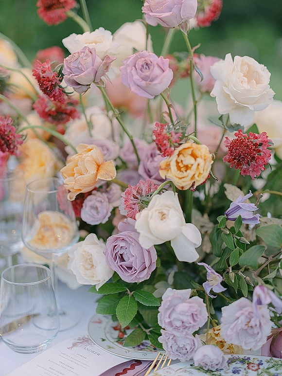 Reception tablescape with a wedding table centerpiece of pink garden roses and greenery, set with patterned plates, gold flatware, and glasses