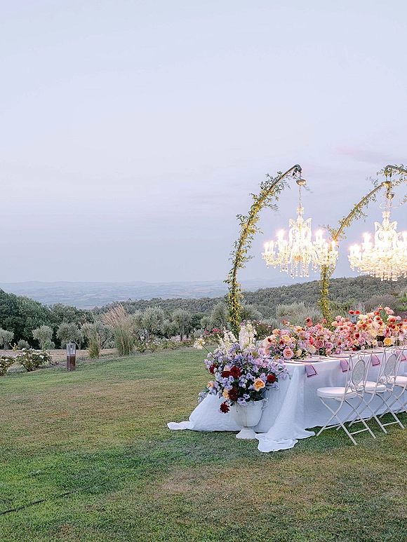 Reception tablescape with an outdoor wedding reception table, taper candles and pastel florals under crystal chandeliers on a grassy lawn