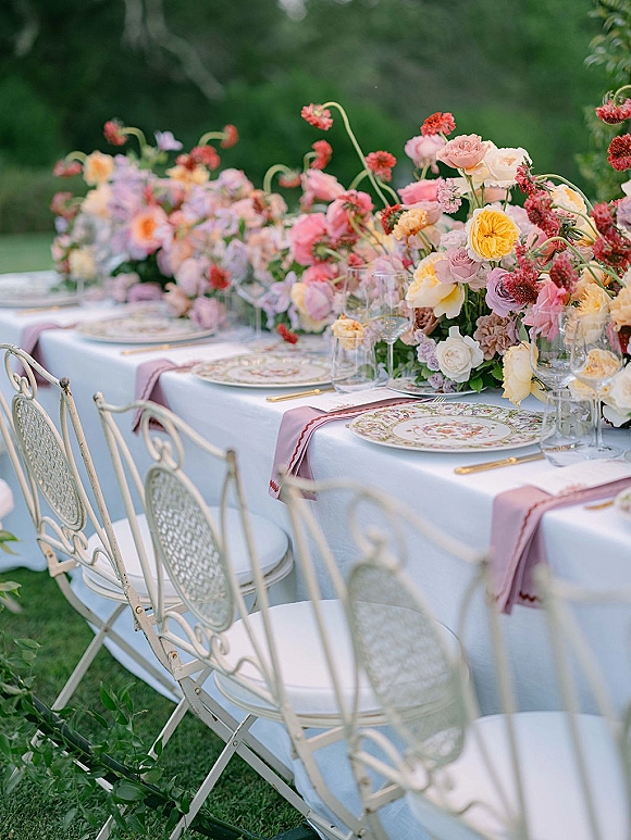 Reception tablescape with outdoor reception table styling, pastel rose and ranunculus runner, patterned plates, gold flatware on lawn