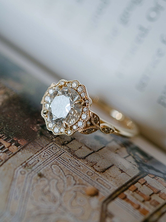 Engagement ring with oval diamond halo ring on a paper map beside invitation paper, gold band and wedding band stacked in detail shot