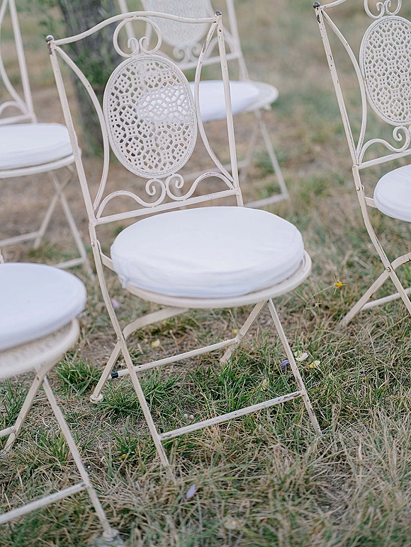 Ceremony chairs with outdoor wedding chair setup in white wrought iron and cushions arranged in rows on a green grass lawn