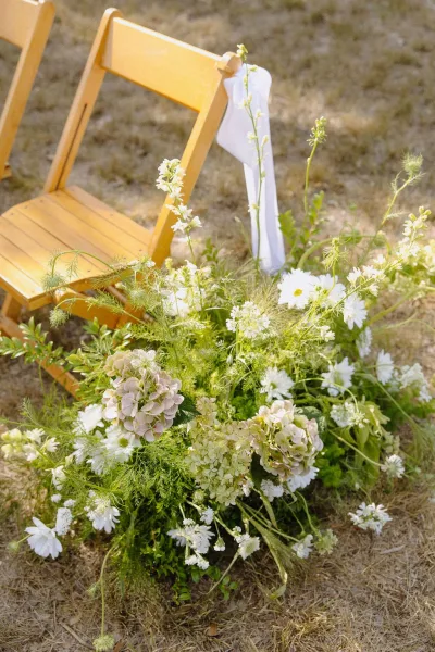 Ceremony aisle flowers line an outdoor ceremony aisle, with hydrangeas clustering along the path on a dry grass lawn.