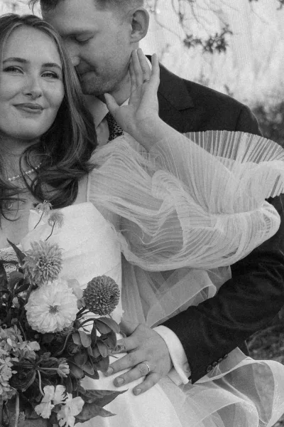 Black and white couple portrait of a bride and groom embracing closely, her ruffled tulle sleeve adding texture.