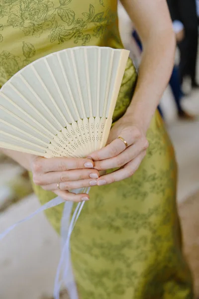 Wedding hand fan, a delicate paper folding fan tied with ribbons, gracefully opened and ready to cool guests.