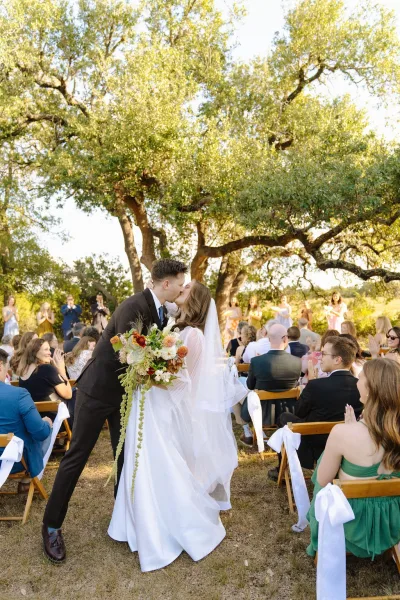 Aisle kiss during a wedding ceremony exit as newlyweds dip in the aisle, her veil trailing while guests cheer