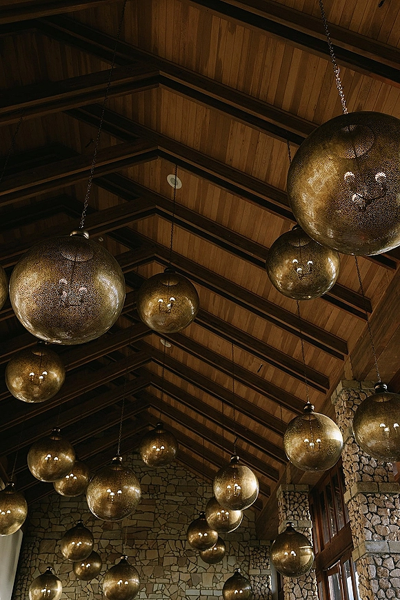 Reception lighting with hanging globe lights suspended by chains, casting warm glow beneath wood beams in a stone-walled venue