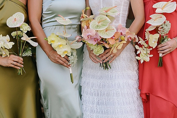 Bridesmaid bouquets with anthurium wedding bouquet and orchids, held by bridesmaids in mismatched dresses against outdoor greenery backdrop