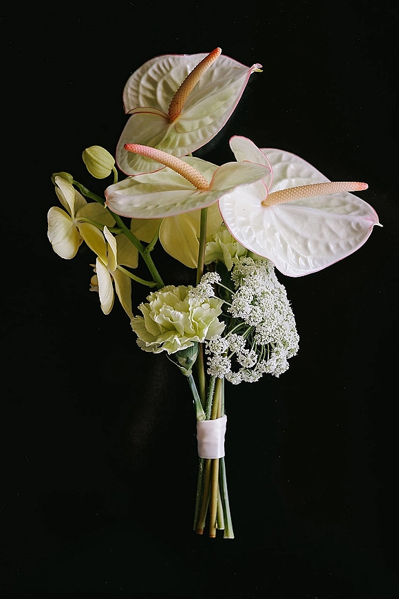 Wedding bouquet with white anthurium and orchids, Queen Anne's lace and carnations, long stems wrapped in white tape on black backdrop