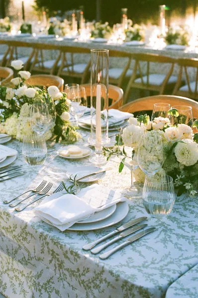Reception tablescape showcasing outdoor reception table decor with taper candles, set among garden trees in warm evening light.