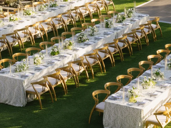 Reception tablescape at an outdoor wedding reception, featuring taper candles lining the tables on a grass lawn.