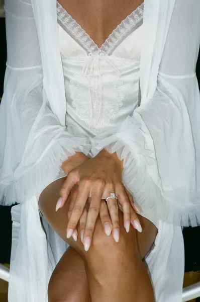 Bridal nails featuring a nude almond manicure, hands gently clasped to showcase an engagement ring during getting ready details.