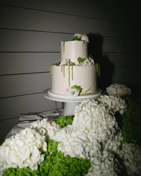 Wedding cake, a smooth buttercream wedding cake adorned with white florals, set against a white shiplap wall.