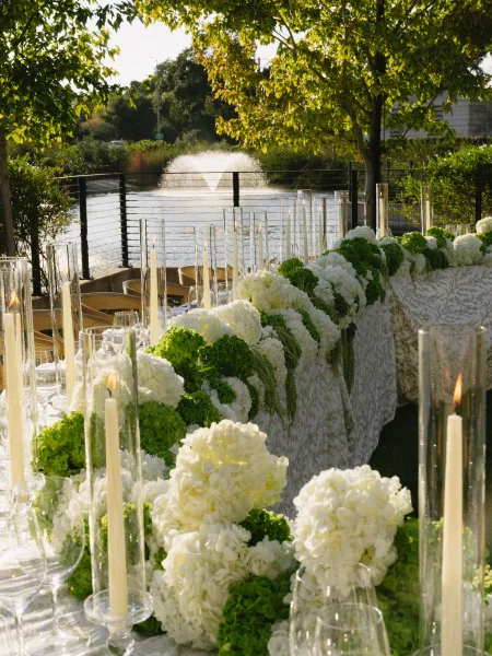 Reception tablescape showcasing outdoor reception decor, featuring hydrangeas, set by a lake with a fountain and trees.