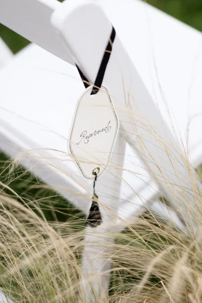 Wedding reserved sign serving as a ceremony seating sign on a white folding chair, tied with a black ribbon by ornamental grasses.