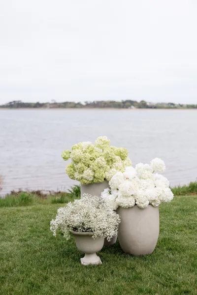 Wedding floral arrangement featuring hydrangea wedding flowers set on a waterfront lawn with distant trees beneath an overcast sky.