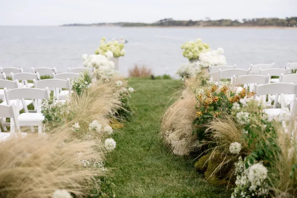 Ceremony aisle design for a waterfront ceremony aisle, with lush ground florals lining a grass lawn beside the shoreline.