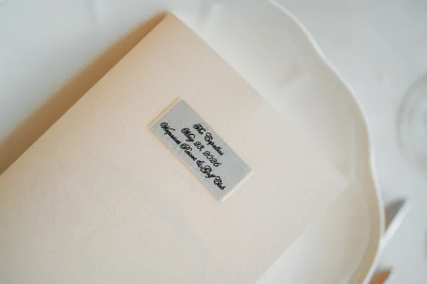 Wedding menu, a menu on plate tied with a ribbon, completes a neutral place setting with clear glassware.