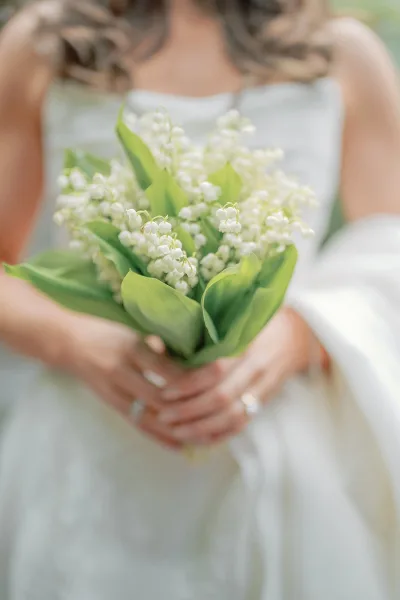 Lily of the valley bouquet, a small bridal bouquet, rests against a classic bridal gown amid lush garden greenery.