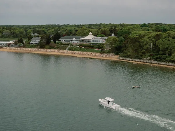Waterfront wedding venue, a coastal wedding venue featuring a glass pavilion overlooking water and shoreline cottages beneath a cloudy sky.