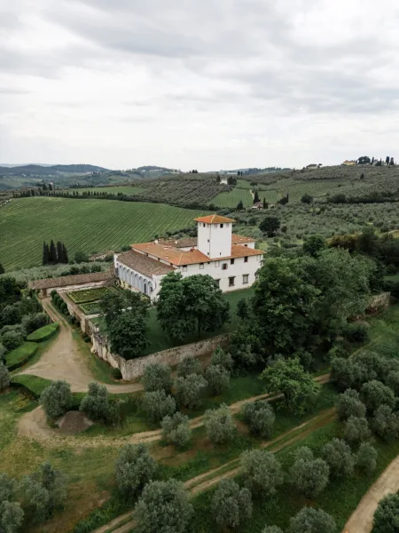 Villa wedding venue nestled in vineyards; this vineyard wedding venue has stone walls amid olive trees and rolling hills under a cloudy sky.