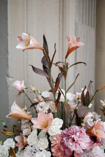 Wedding floral arrangement of blush and white florals featuring lilies, set against a stone wall and an architectural column.