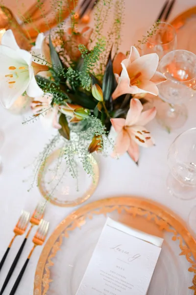 Wedding place setting with a gold charger plate anchoring the arrangement, styled in a modern, elegant look for a chic reception table.