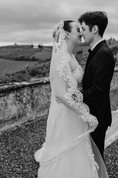 Couple portrait of an almost kiss wedding photo as the bride and groom embrace before vineyard hills, her lace veil softly framing their faces.
