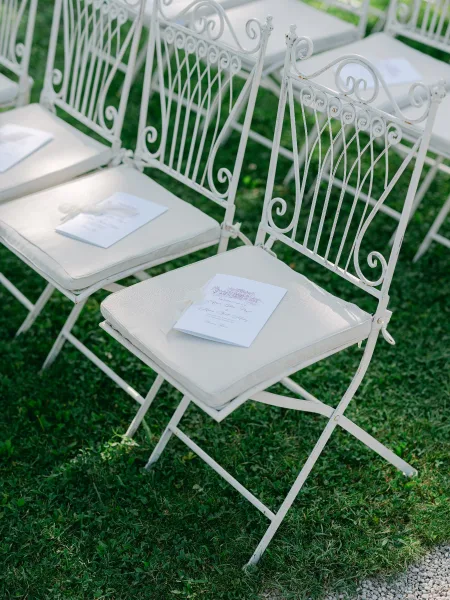 Ceremony seating features garden ceremony chairs arranged on a grass lawn with ribbon-tied programs set neatly on each seat.
