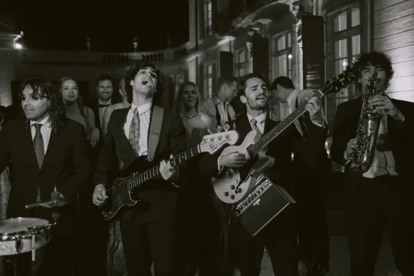 Wedding band performance at a nighttime wedding reception, a saxophonist leading in an outdoor courtyard beneath a historic facade.