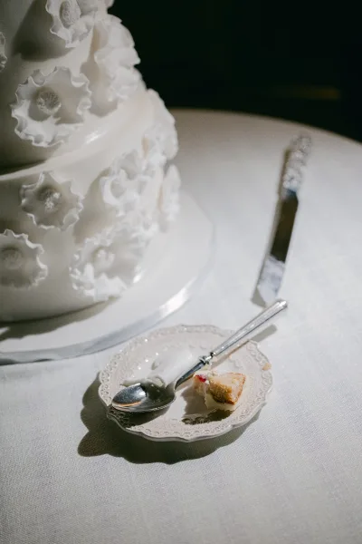 Wedding cake, the fondant wedding cake adorned with delicate sugar flowers, set on a linen-draped table against a softly shadowed dark backdrop.