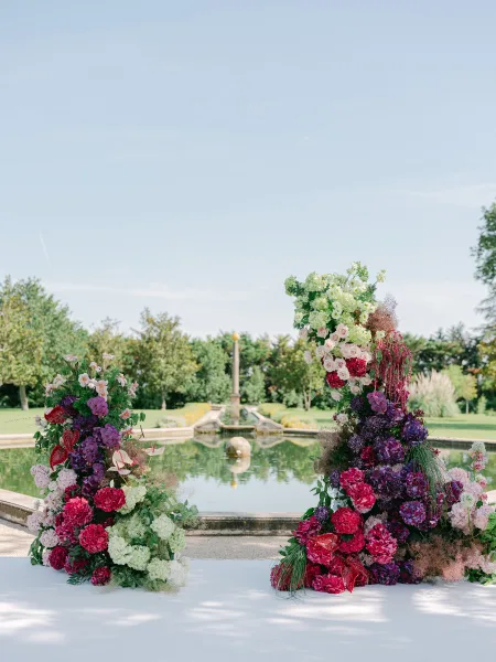 Outdoor ceremony decor featuring lush garden ceremony flowers and flower pillars beside a reflecting pool and fountain.