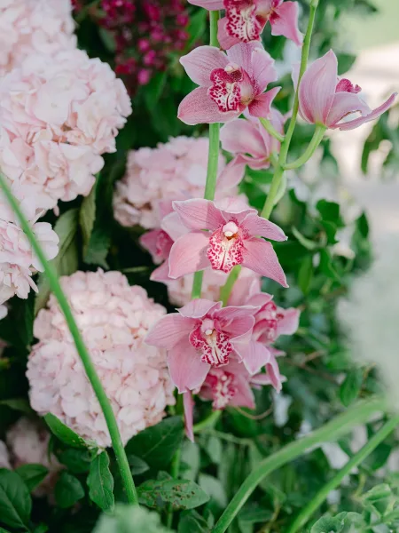 Wedding flowers in a lush floral arrangement featuring pink orchids, set against a leafy garden backdrop with soft, natural light.