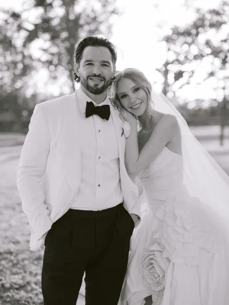 Couple portrait, an outdoor wedding portrait with the bride leaning on the groom, floral appliqué catching light as they stand close.
