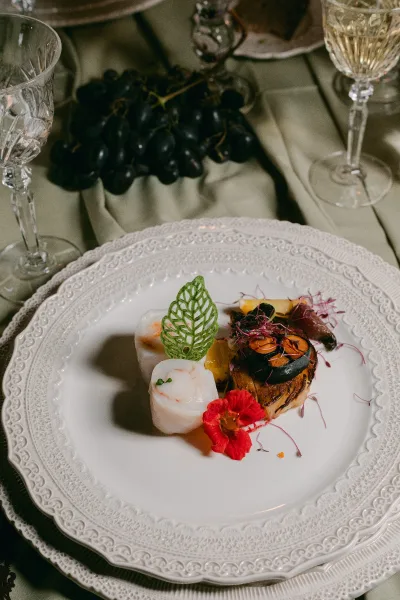 Wedding plated entree artfully arranged with edible flowers for a plated reception dinner, set on a green tablecloth.