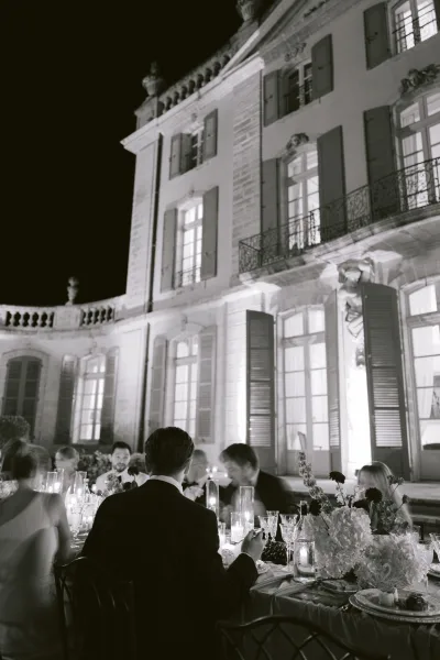 Reception tablescape at an outdoor dinner reception, glowing with candles, set before a historic mansion facade under a velvet night sky.