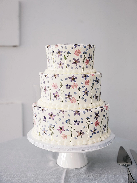 Wedding cake with three tier wedding cake design, floral print icing and buttercream piping on a white stand beside a cake knife