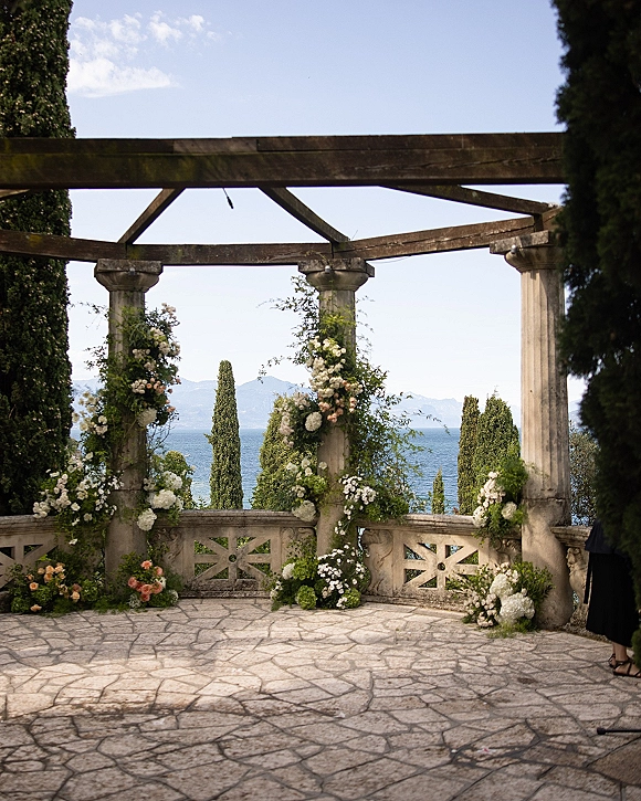 Wedding ceremony arch with outdoor wedding altar styling on a stone pergola, framed by white and blush florals with ocean and mountains beyond