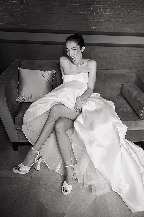 Bridal portrait of a bride sitting on sofa in a strapless gown with tulle underskirt, pearl necklace, and wedding ring in a paneled room