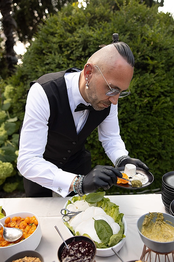 Wedding catering server in a black vest and gloves plating wedding caterer plating appetizers on black plates at a garden buffet table